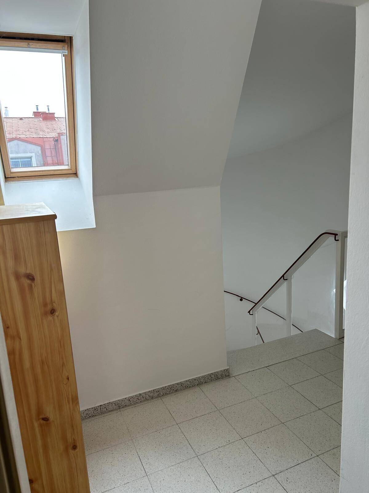 Treppenhaus mit Fliesenboden, weiß gestrichenen Wänden und einem Dachfenster für natürliches Licht.
