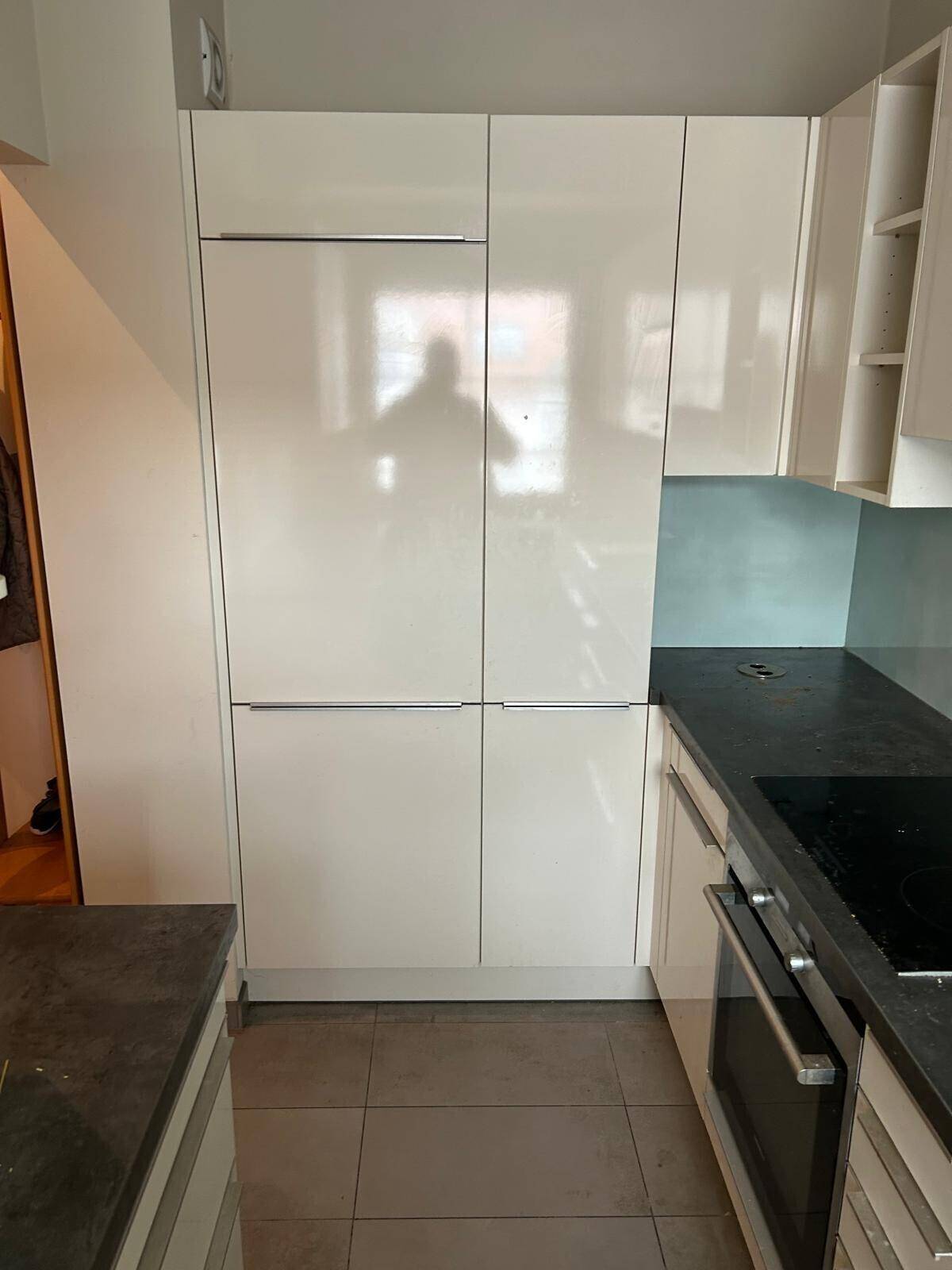 Moderne Küche mit weißen Hochglanzschränken und einem integrierten Kühlschrank.
