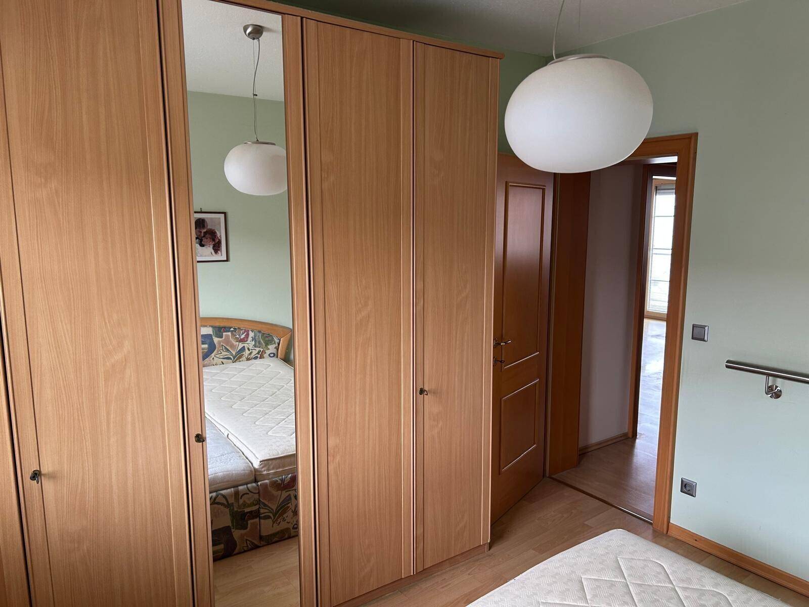 Schlafzimmer mit Holzschränken, einem Bett und einem Spiegel, der den Raum optisch vergrößert.