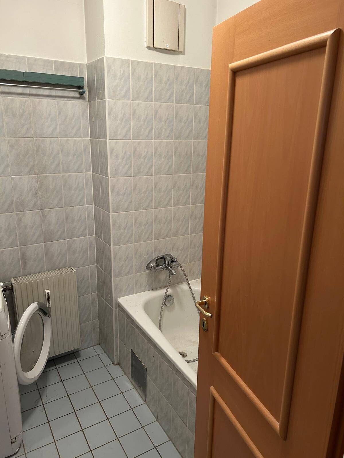Badezimmer mit Badewanne, hellblauen Fliesen und einem Heizkörper, der auch als Handtuchhalter dient.