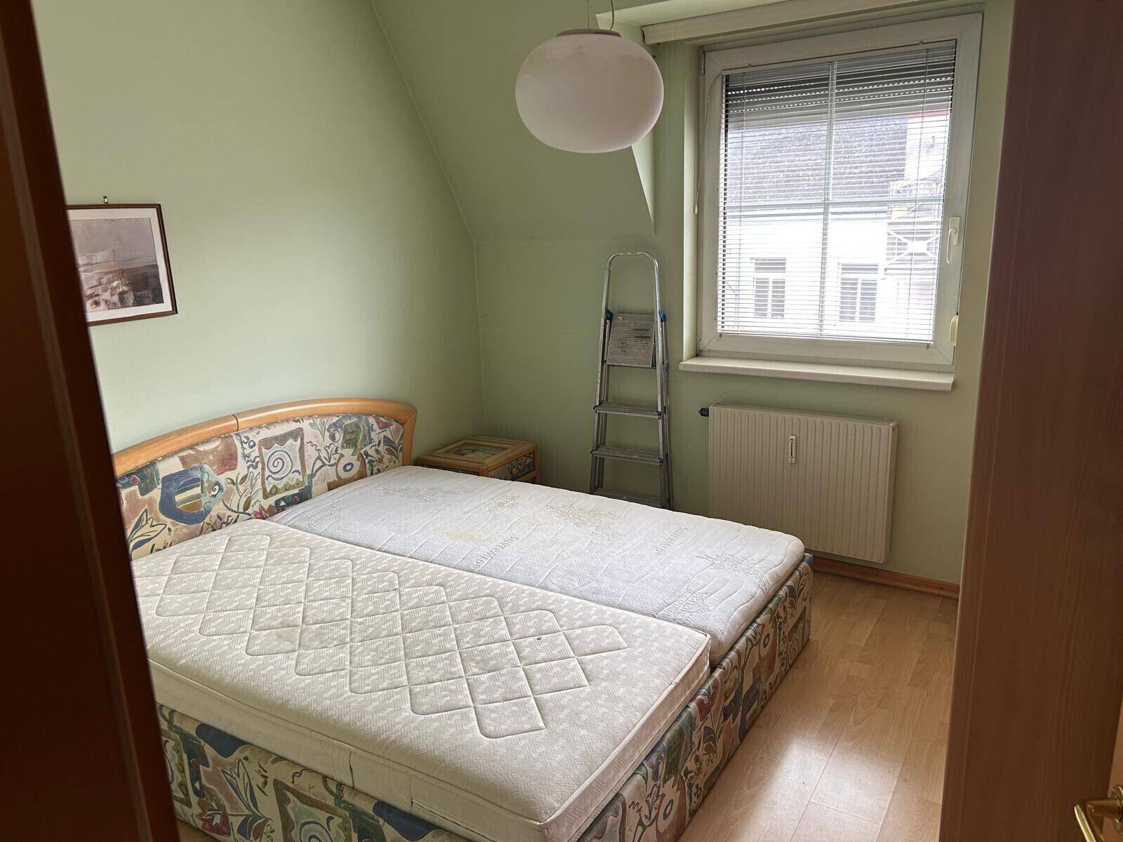 Schlafzimmer mit zwei Einzelbetten, einem Fenster und hellgrünen Wänden unter einer Dachschräge.