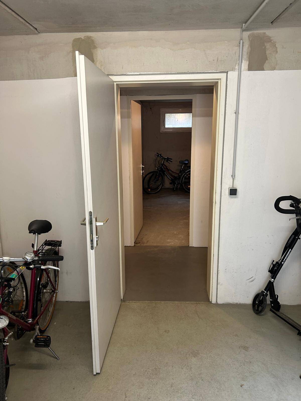 Kellerraum mit Fahrrädern und einer offenen Tür, die zu weiteren Räumen führt.