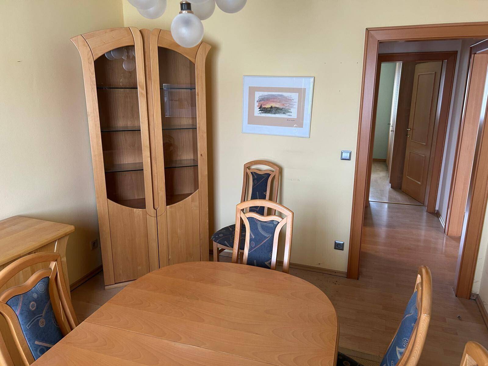 Esszimmer mit Holzboden, einem ovalen Esstisch und einem Vitrinenschrank, der den Raum schmückt.