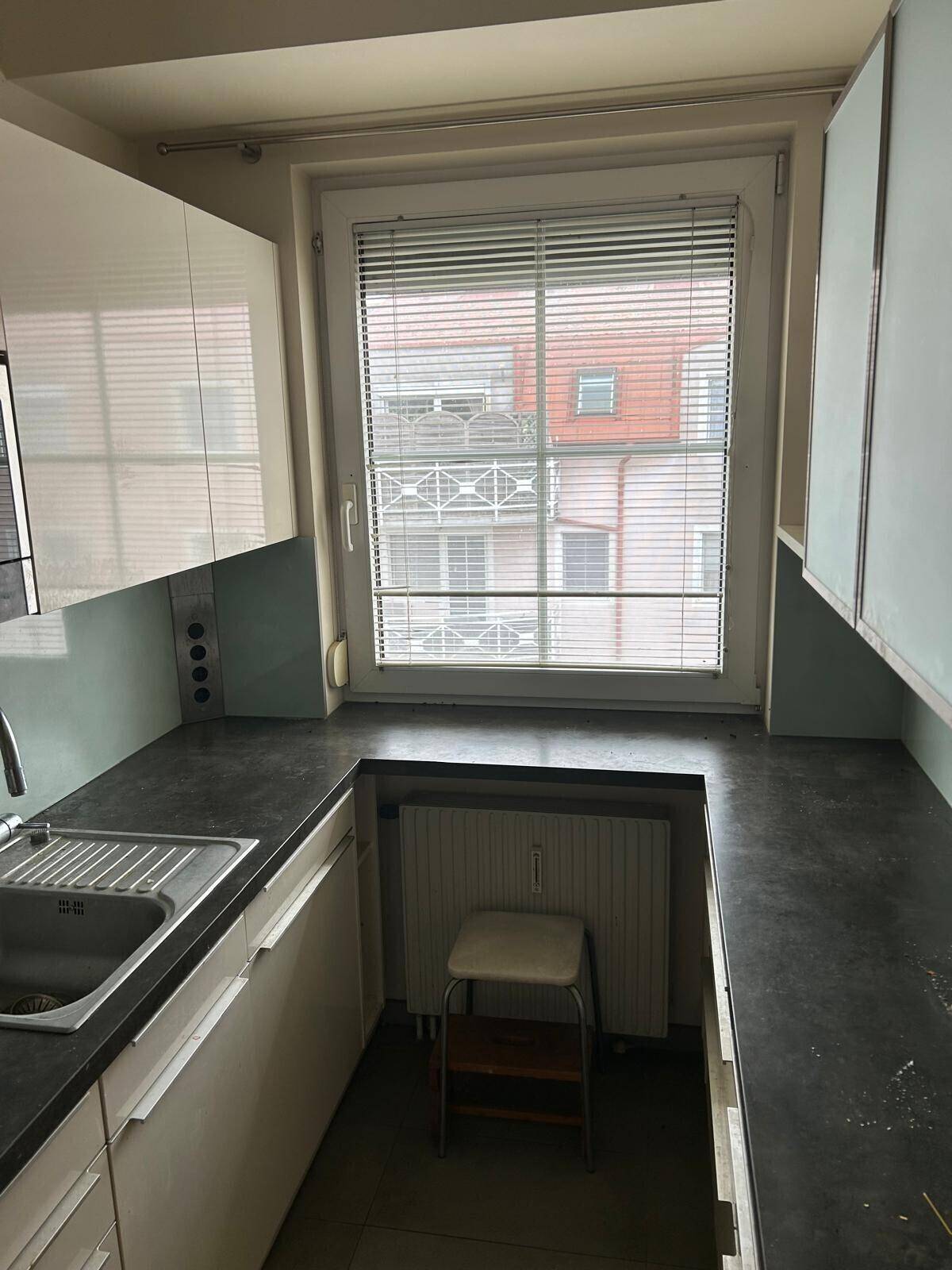 Küchenzeile mit dunkler Arbeitsplatte, Spüle und einem Fenster, das Tageslicht hereinlässt.