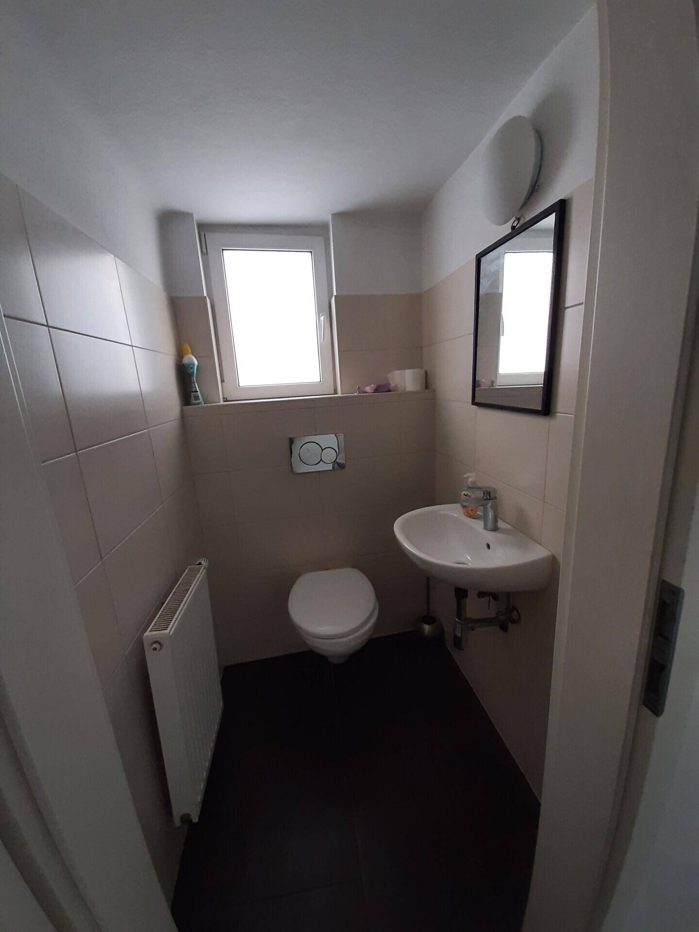 Kleines Gäste-WC mit Wand-WC, Waschbecken und Fenster für natürliche Belüftung.