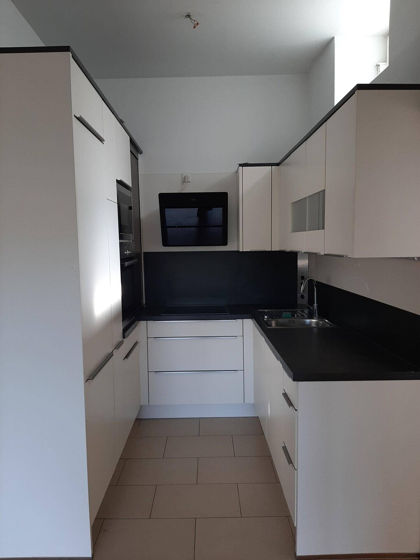 Moderne Einbauküche mit weißen Schränken, dunkler Arbeitsplatte und integrierten Geräten.