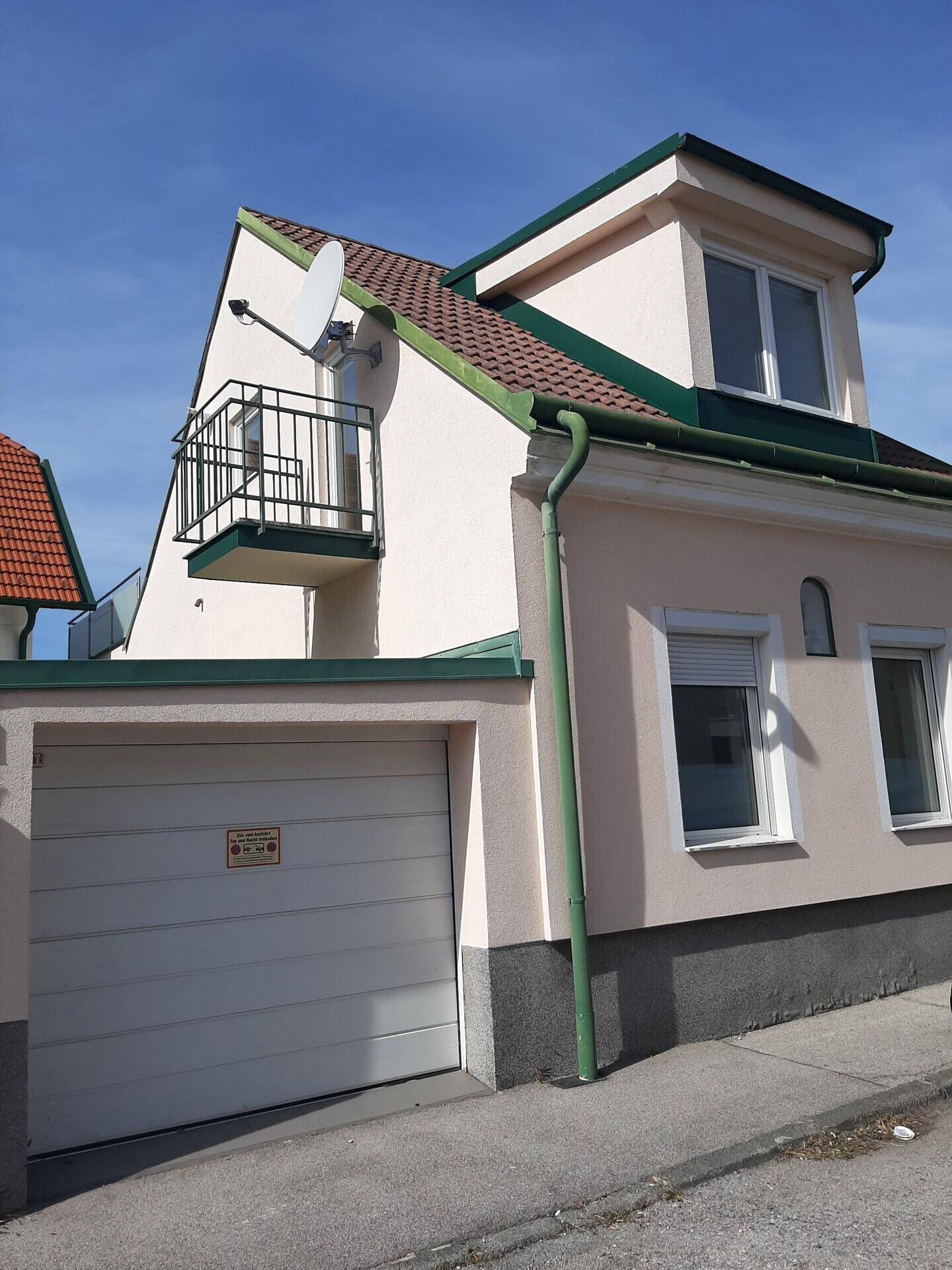 Fassade eines Stadthauses mit integrierter Garage und kleinem Balkon im Obergeschoss.