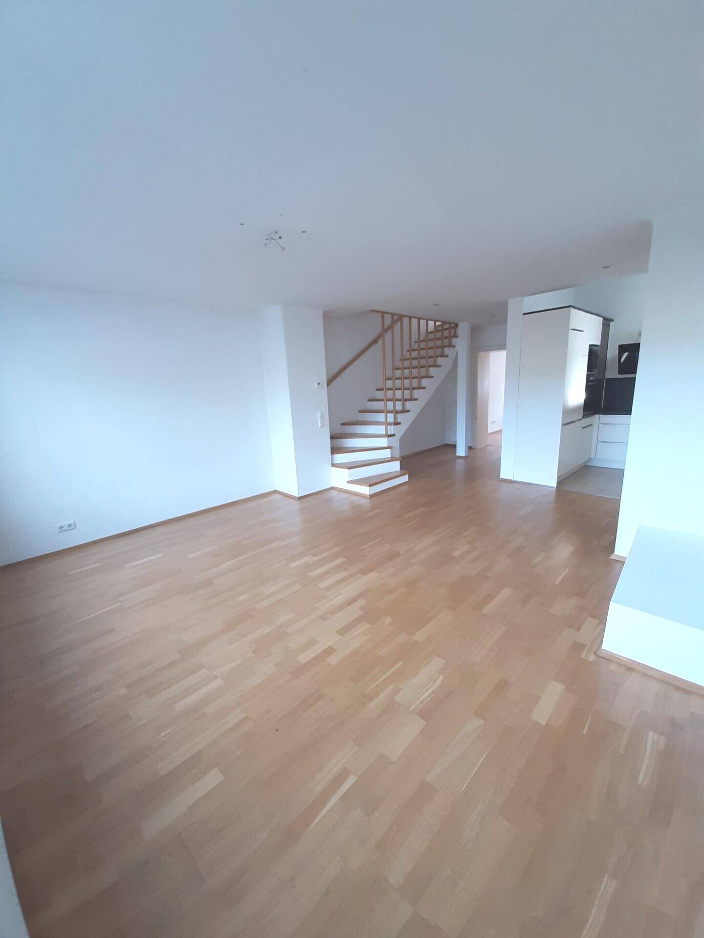 Geräumiges Wohnzimmer mit hellem Parkettboden und offener Treppe zum Obergeschoss.