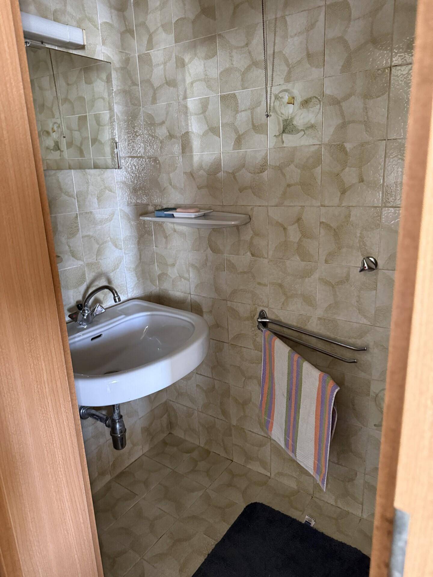 Kleines Badezimmer mit beigen Fliesen, Waschbecken und einem Spiegelschrank.