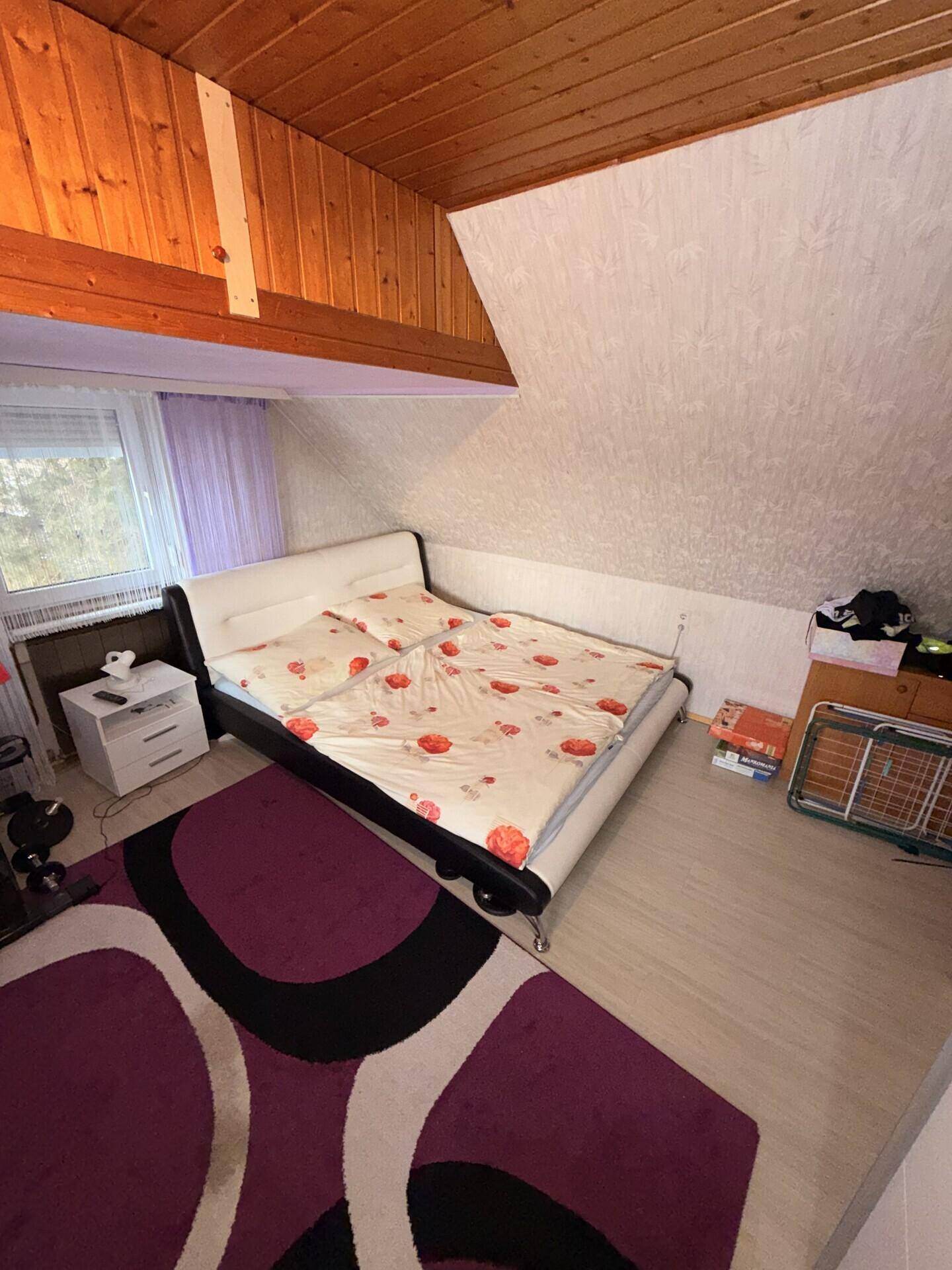 Dachgeschoss-Schlafzimmer mit Dachschrägen, Holzverkleidung und Bett in gemütlichem Ambiente.