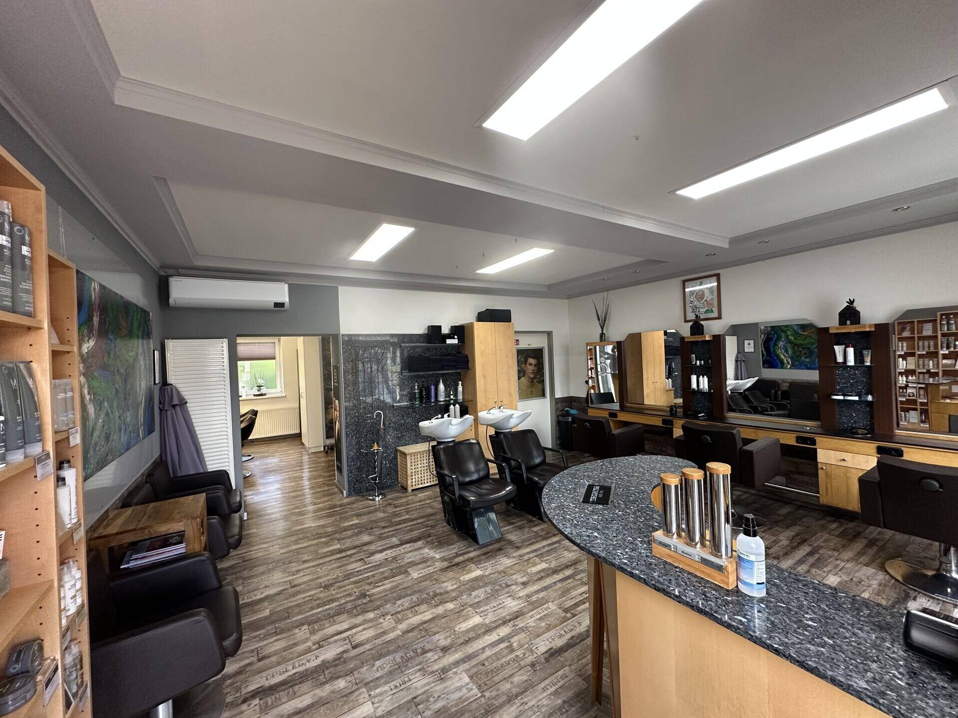 Geräumiger Friseursalon mit mehreren Bedienplätzen und Haarwaschbecken.
