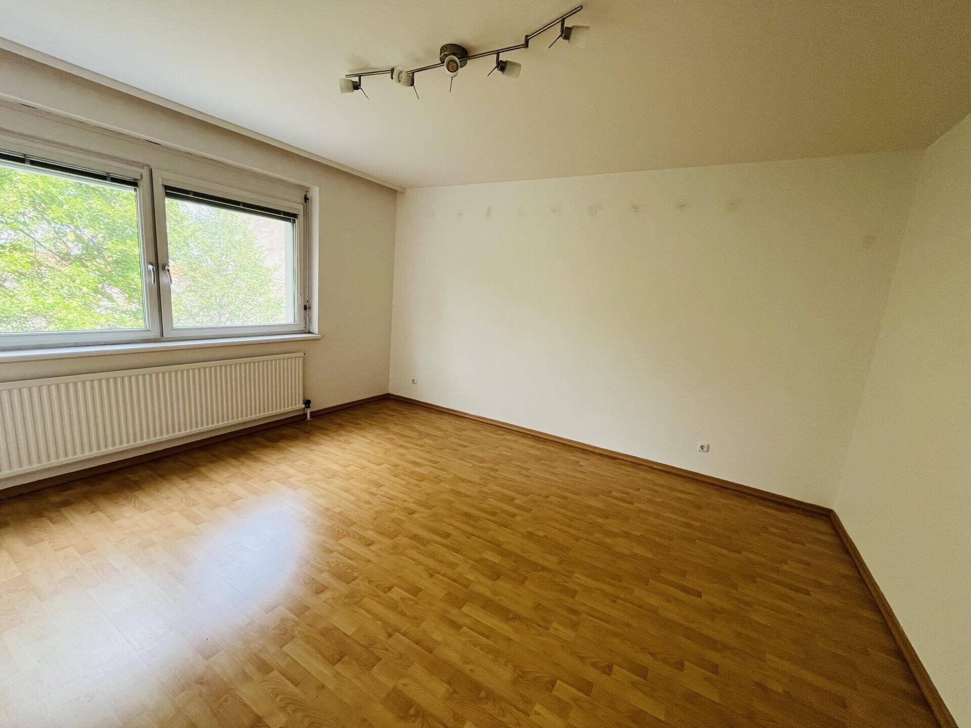 Geräumiges Schlafzimmer mit Parkettboden und Blick ins Grüne.