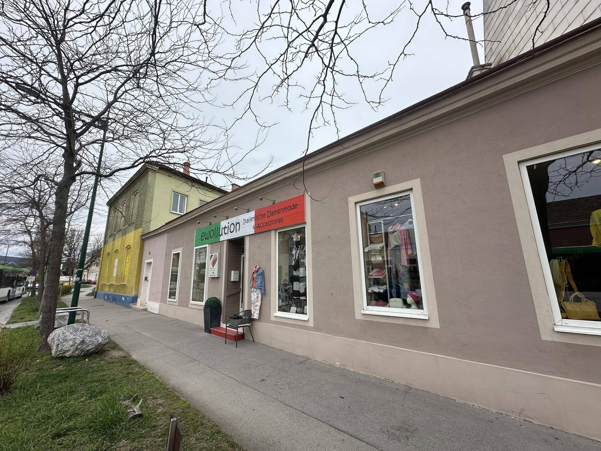 Angrenzendes Gebäude mit Ladenfronten und Bäumen entlang des Bürgersteigs.