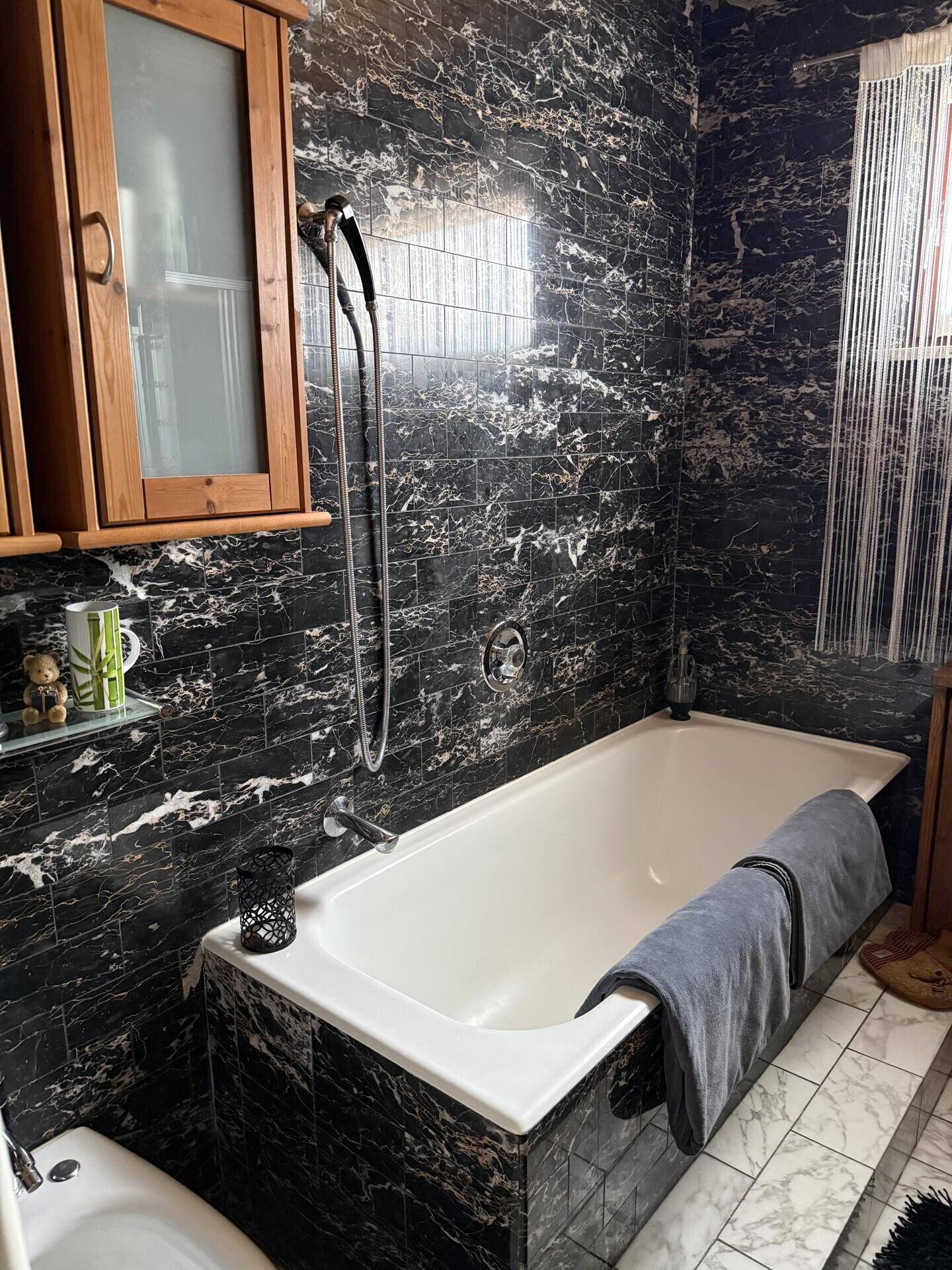 Badezimmer mit dunklen Marmorfliesen, Badewanne und Fenster.