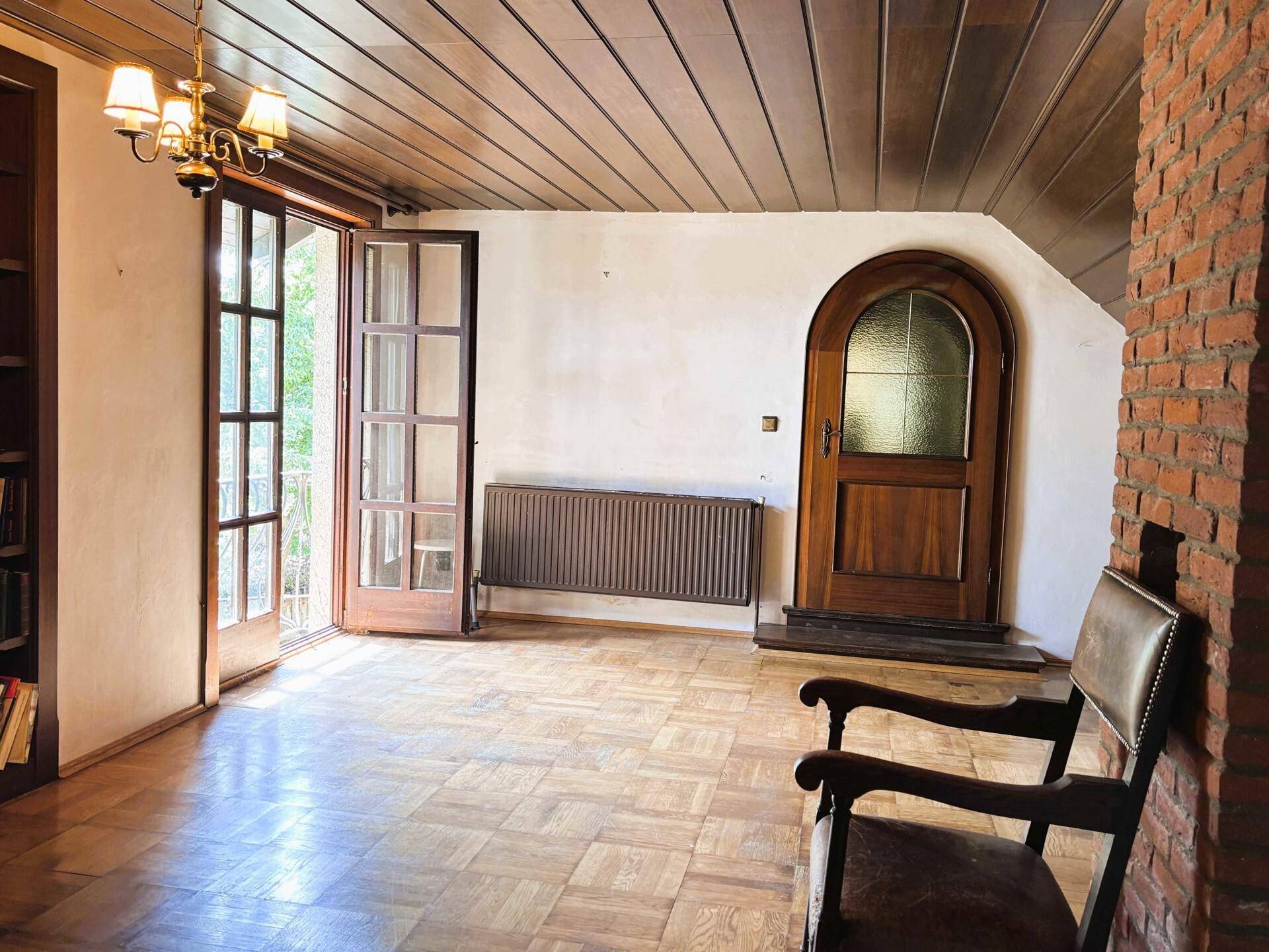 Heller Raum mit Holzboden, Holzbalkendecke und Zugang zu einem französischen Balkon.