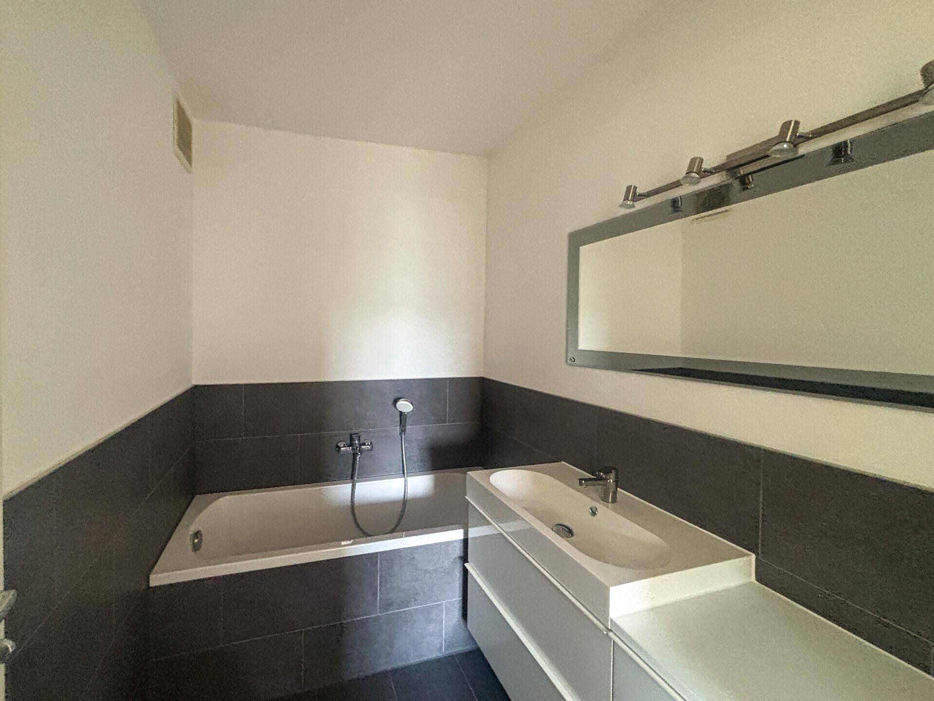 Modernes Badezimmer mit Badewanne, Waschtisch und großem Spiegel, in Grau und Weiß gehalten.