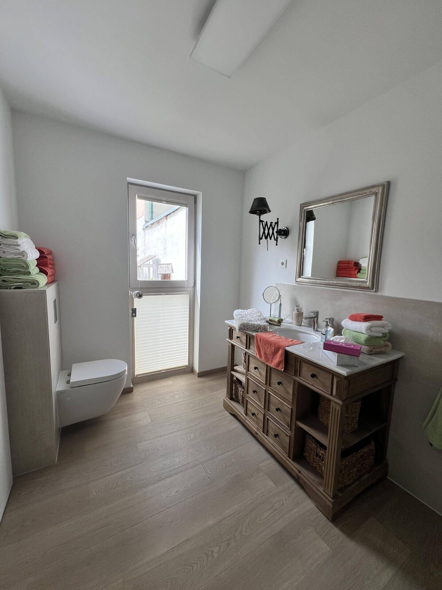 Helles Badezimmer mit Fenster, wandhängendem WC und elegantem Waschtischunterschrank.