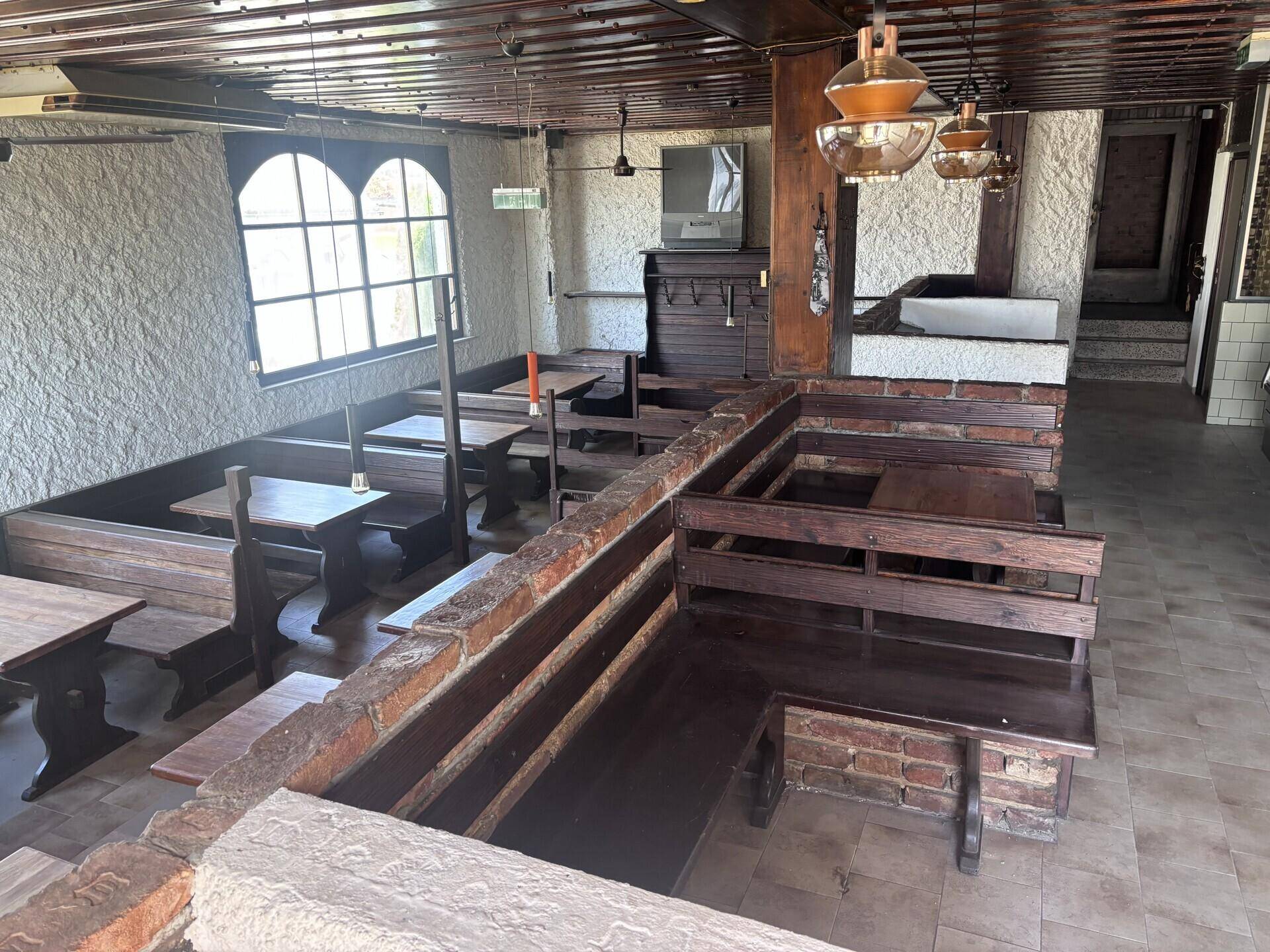 Rustikaler Gastraum mit dunklen Holzbänken, Tischen und Steinwänden, ausgestattet mit traditionellen Leuchten.