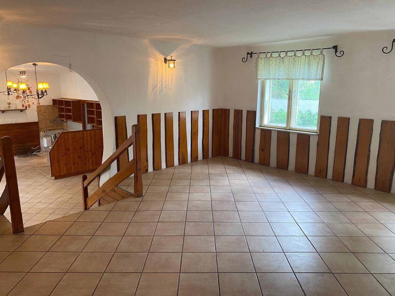 Heller Raum mit Fliesenboden, Holzvertäfelung und einem Rundbogen, der zwei Bereiche verbindet.