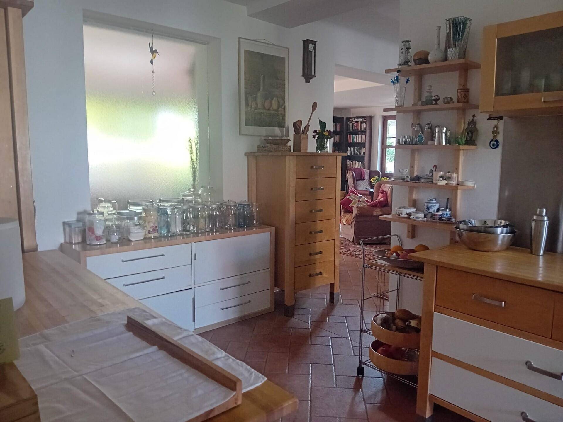 Helle Küche mit Holz-Arbeitsplatten, weißen Schränken und Terrakottaboden, offen zum Wohnbereich.