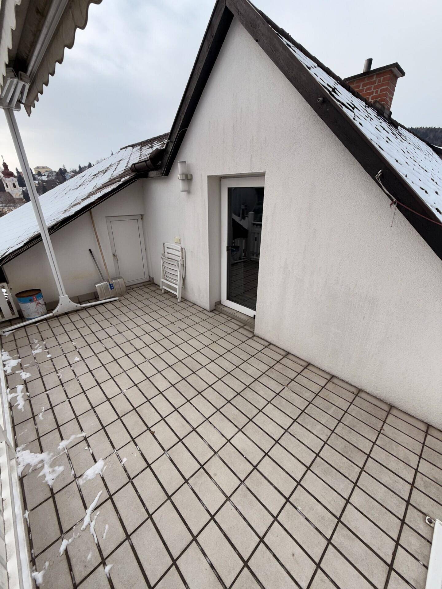 Leere geflieste Terrasse im Winter mit Schneeresten und Blick auf die Umgebung.