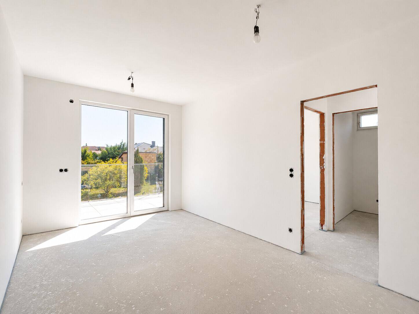 Heller, unfertiger Raum mit großem Fenster und Zugang zu einem weiteren Zimmer, ideal für Schlaf- oder Arbeitszimmer.