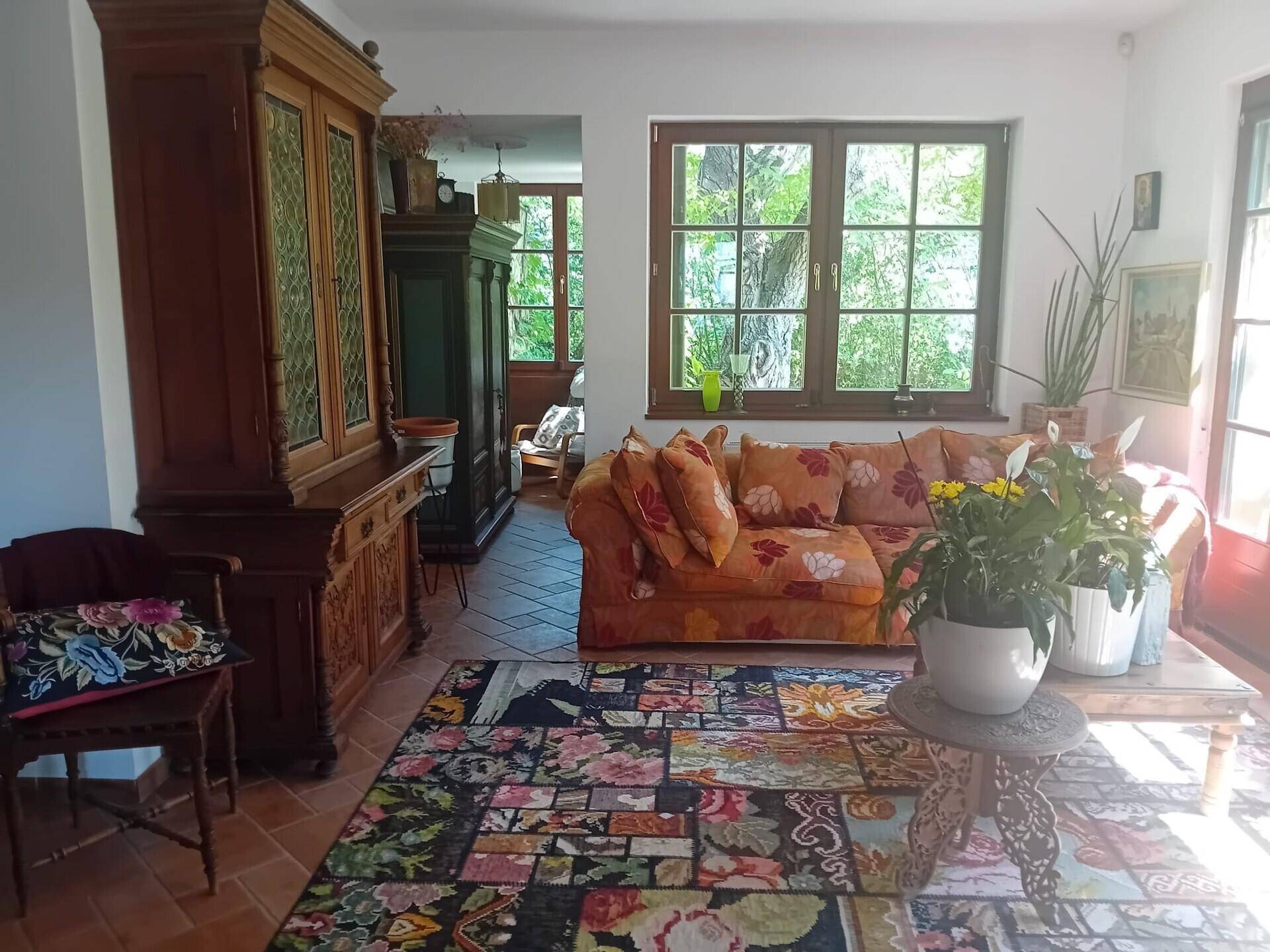 Gemütliches Wohnzimmer mit floralem Sofa, antiken Möbeln und Terrakottaboden, mit Blick ins Grüne.