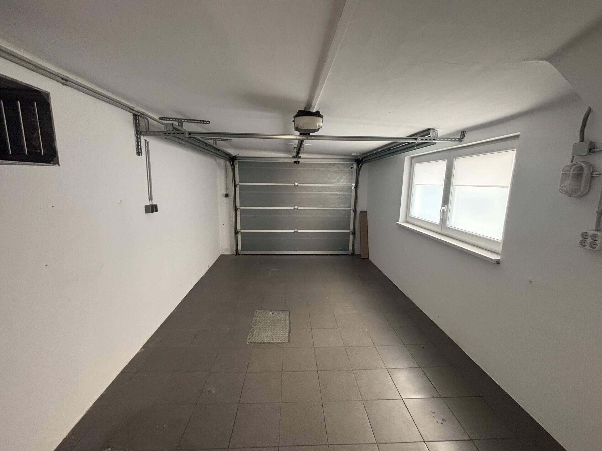 Geräumige Garage mit Fliesenboden, Rolltor und einem Fenster für Tageslicht.