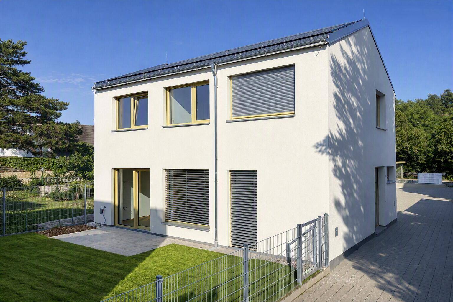 Modernes Einfamilienhaus mit weißer Fassade, Garten und Terrasse unter blauem Himmel.