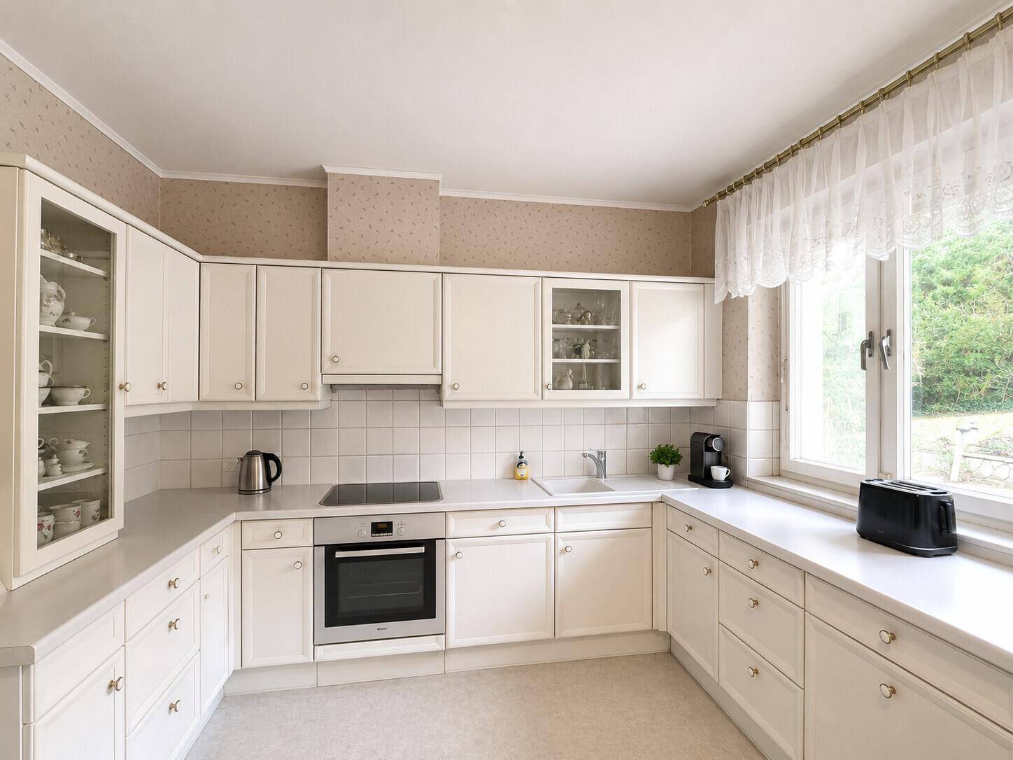 Helle Einbauküche in Weiß mit Induktionskochfeld, Backofen und Fenster zum Garten.