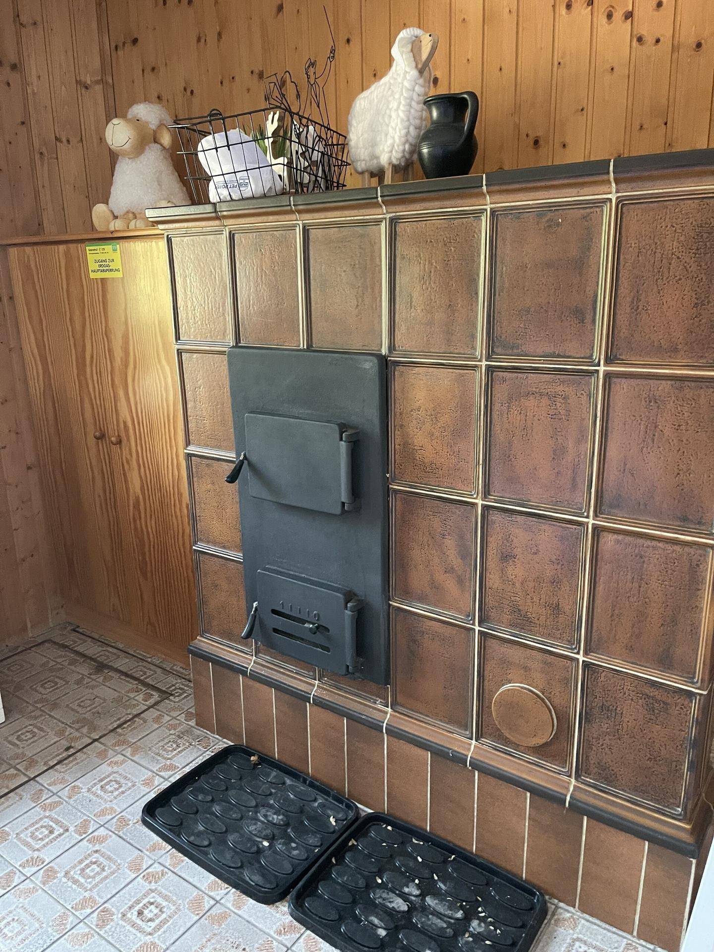 Brauner Kachelofen in einem holzvertäfelten Raum mit Fliesenboden.