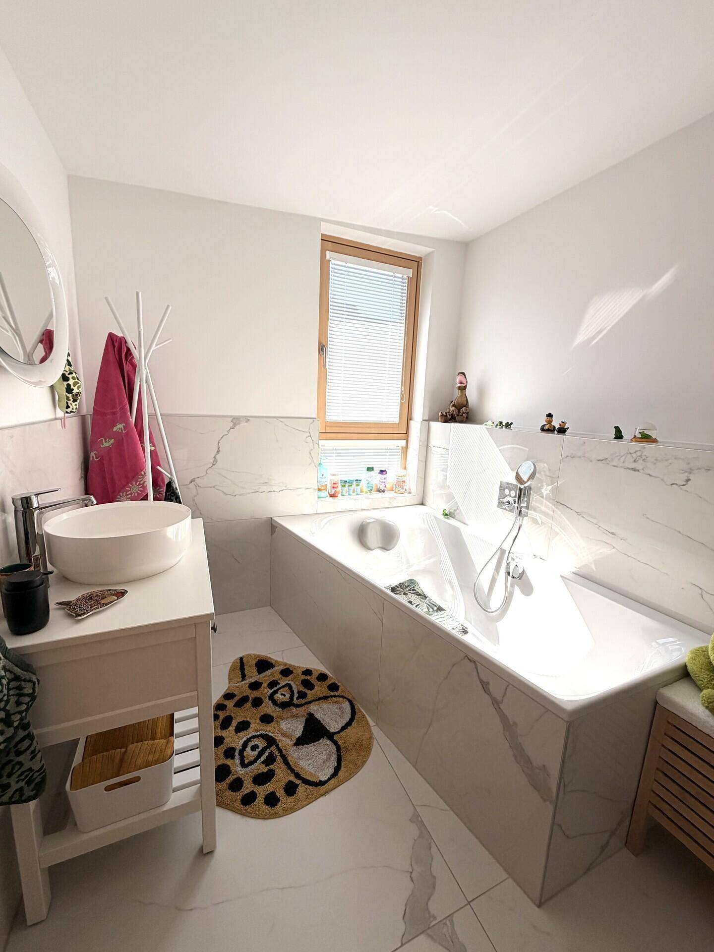 Helles Badezimmer mit Badewanne, runden Spiegel und weißen Marmorfliesen.