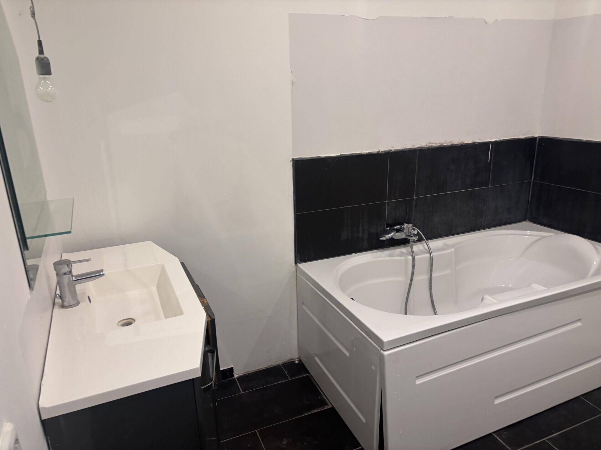 Badezimmer mit einer Badewanne, einem modernen Waschtisch und schwarzen Wand- und Bodenfliesen.