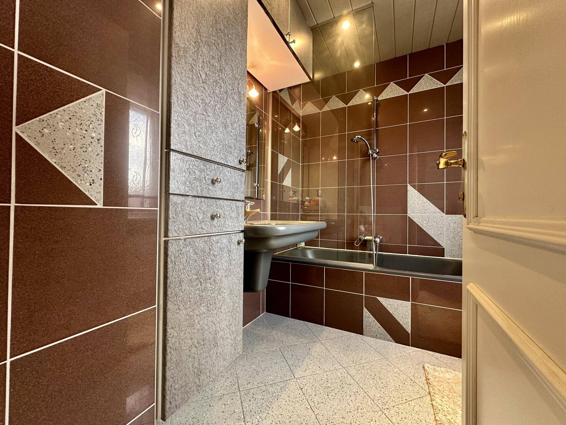 Badezimmer mit braunen Fliesen, Badewanne und Waschbecken.