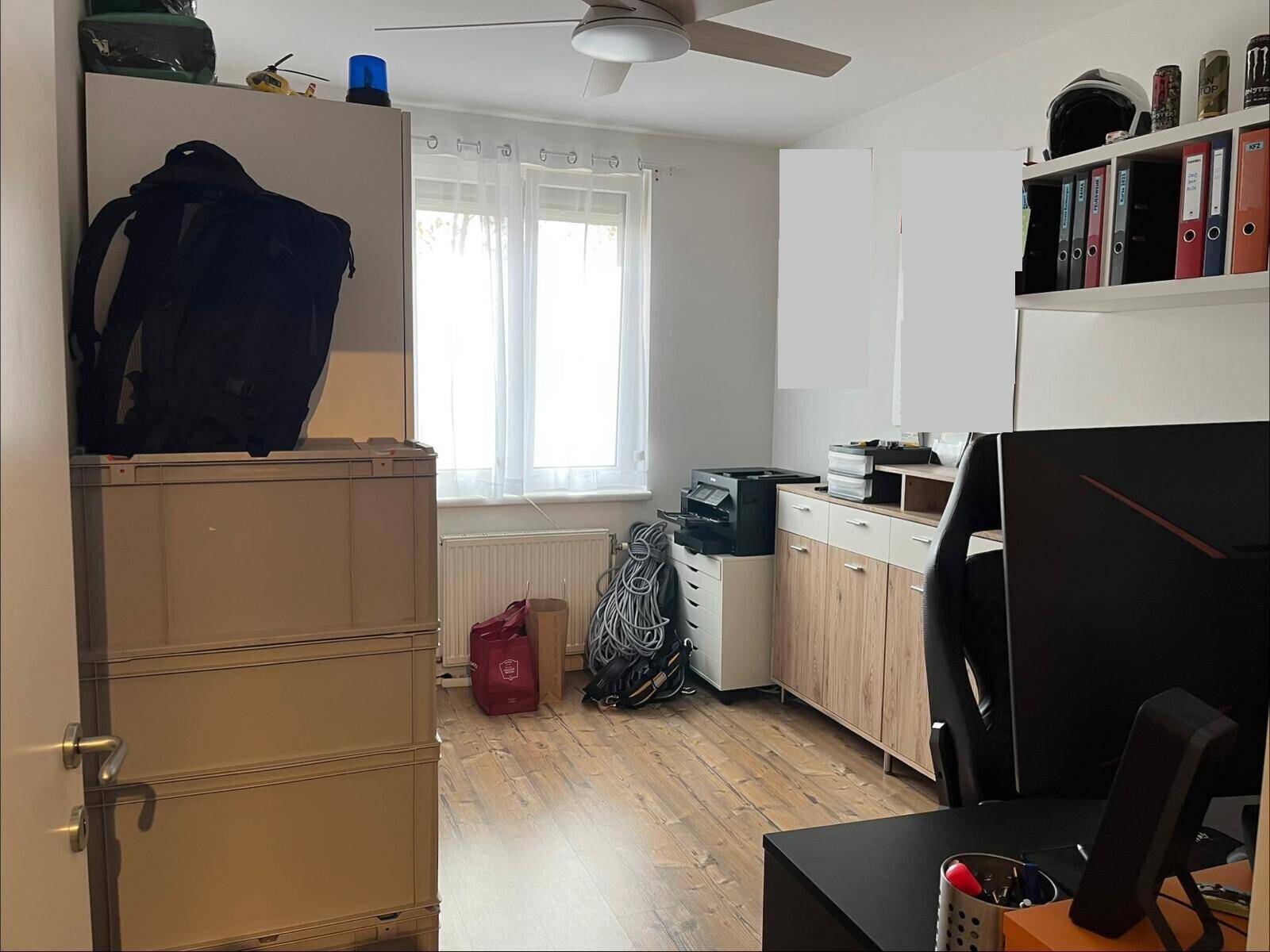 Helles Büro mit Holzfußboden, Deckenventilator und praktischen Lagermöglichkeiten am Fenster.