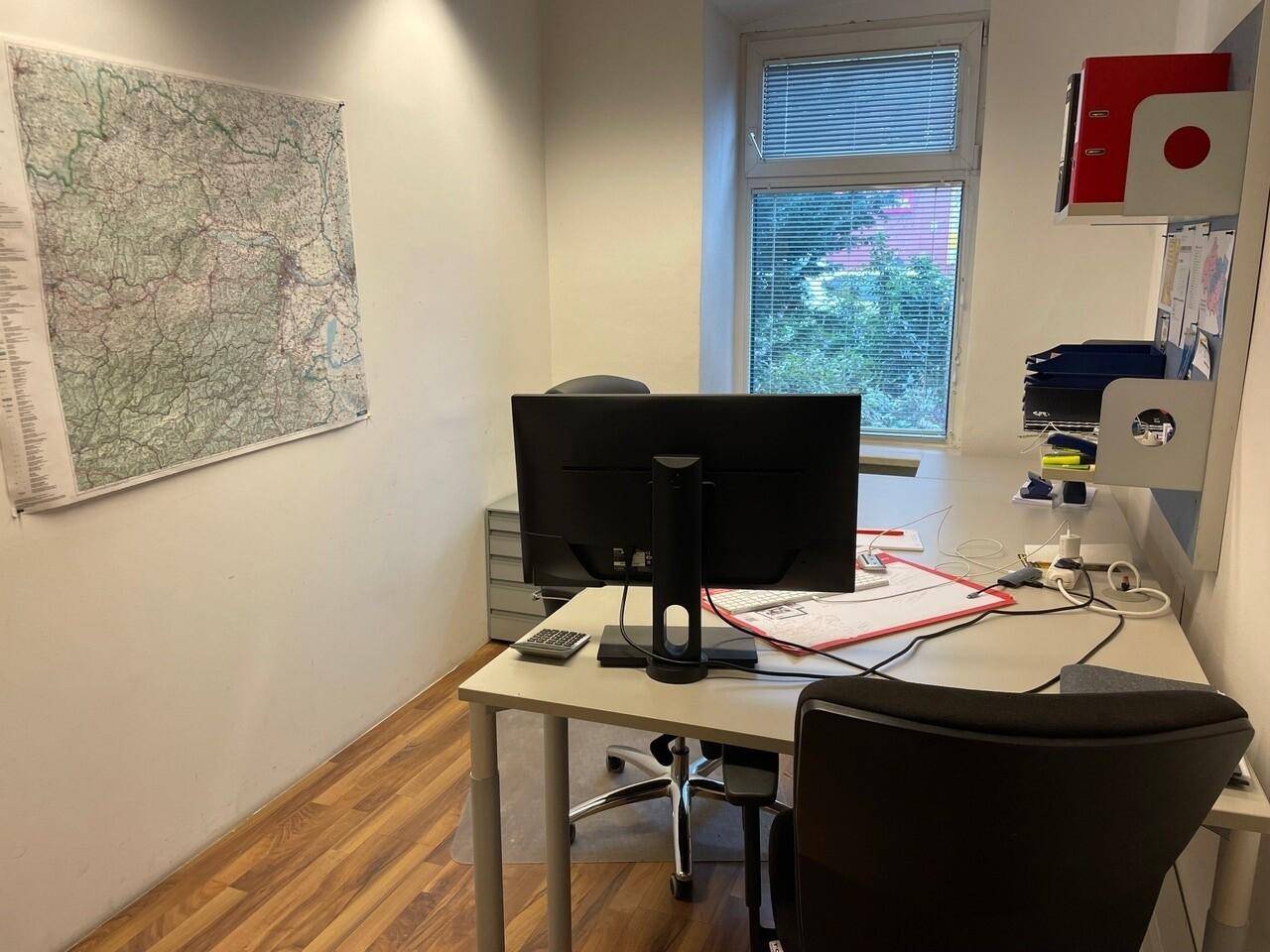 Kleines Büro mit Schreibtisch, Computer und einer großen Karte an der Wand, mit Blick ins Grüne.