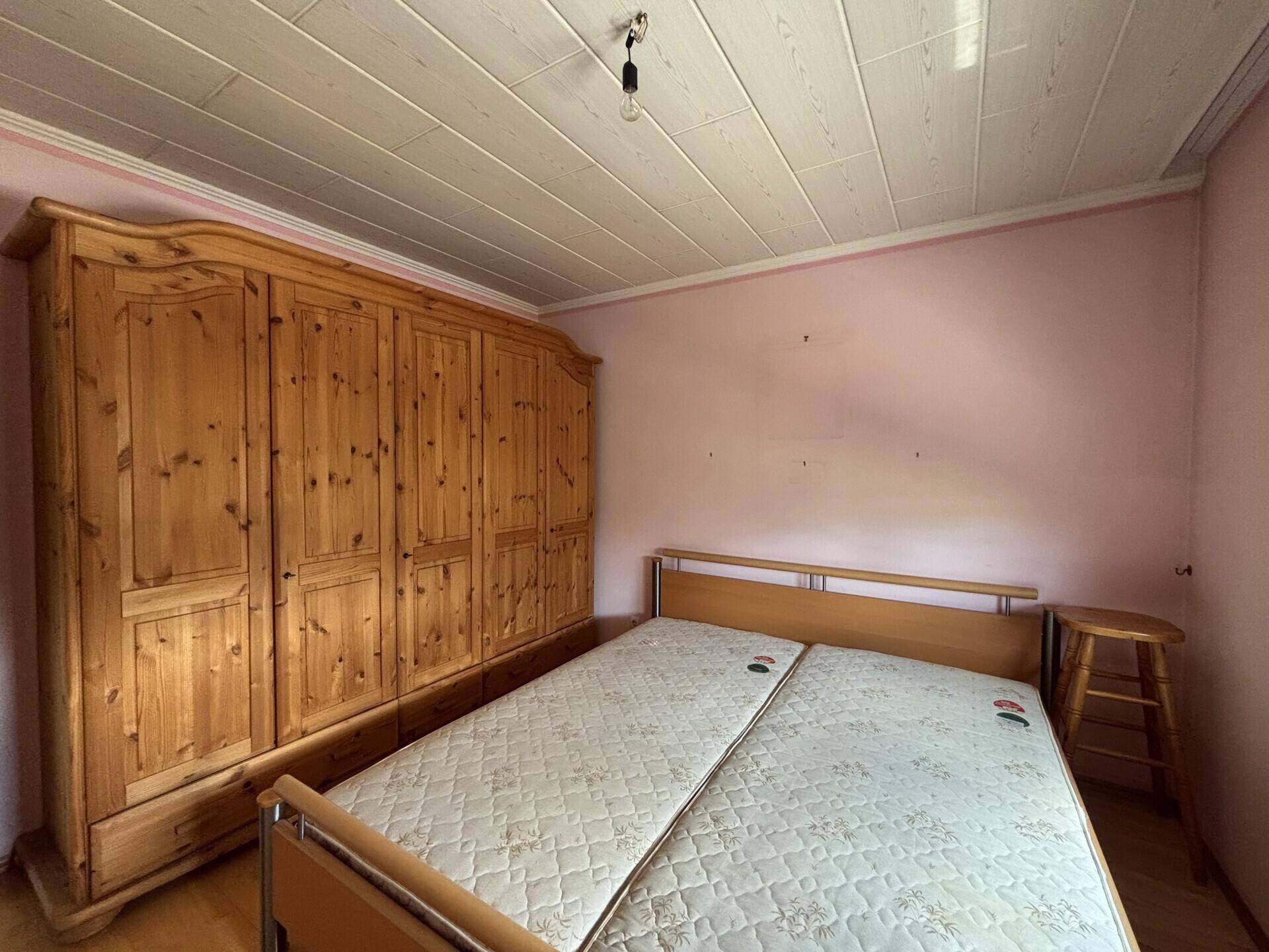Schlafzimmer mit großem Holzschrank und Doppelbett, bereit zur individuellen Gestaltung.