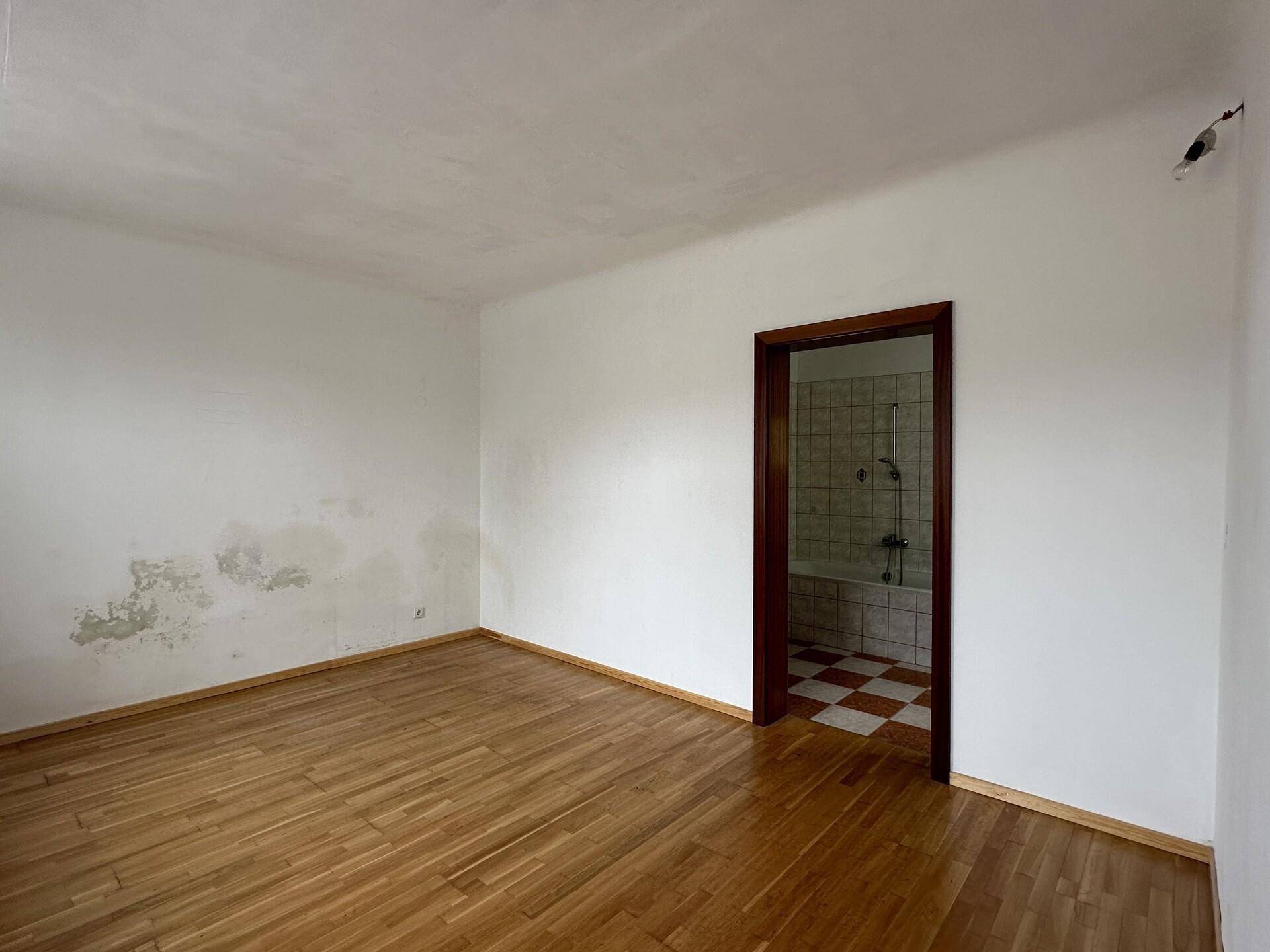 Schlafzimmer mit Holzboden und sichtbaren Gebrauchsspuren an den Wänden.