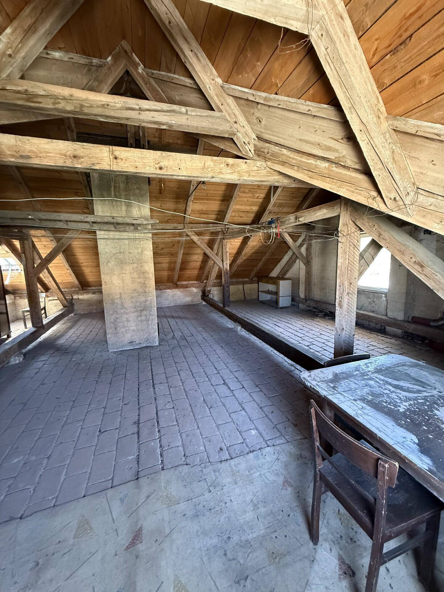 Heller Dachboden mit freiliegenden Holzbalken und rustikalem Ziegelboden, ideal für Umbau.
