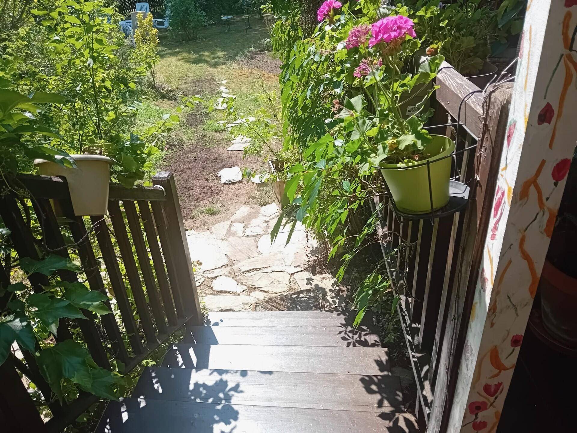 Holztreppe führt hinunter zu einem Steinweg, umgeben von blühenden Pflanzen im Garten.