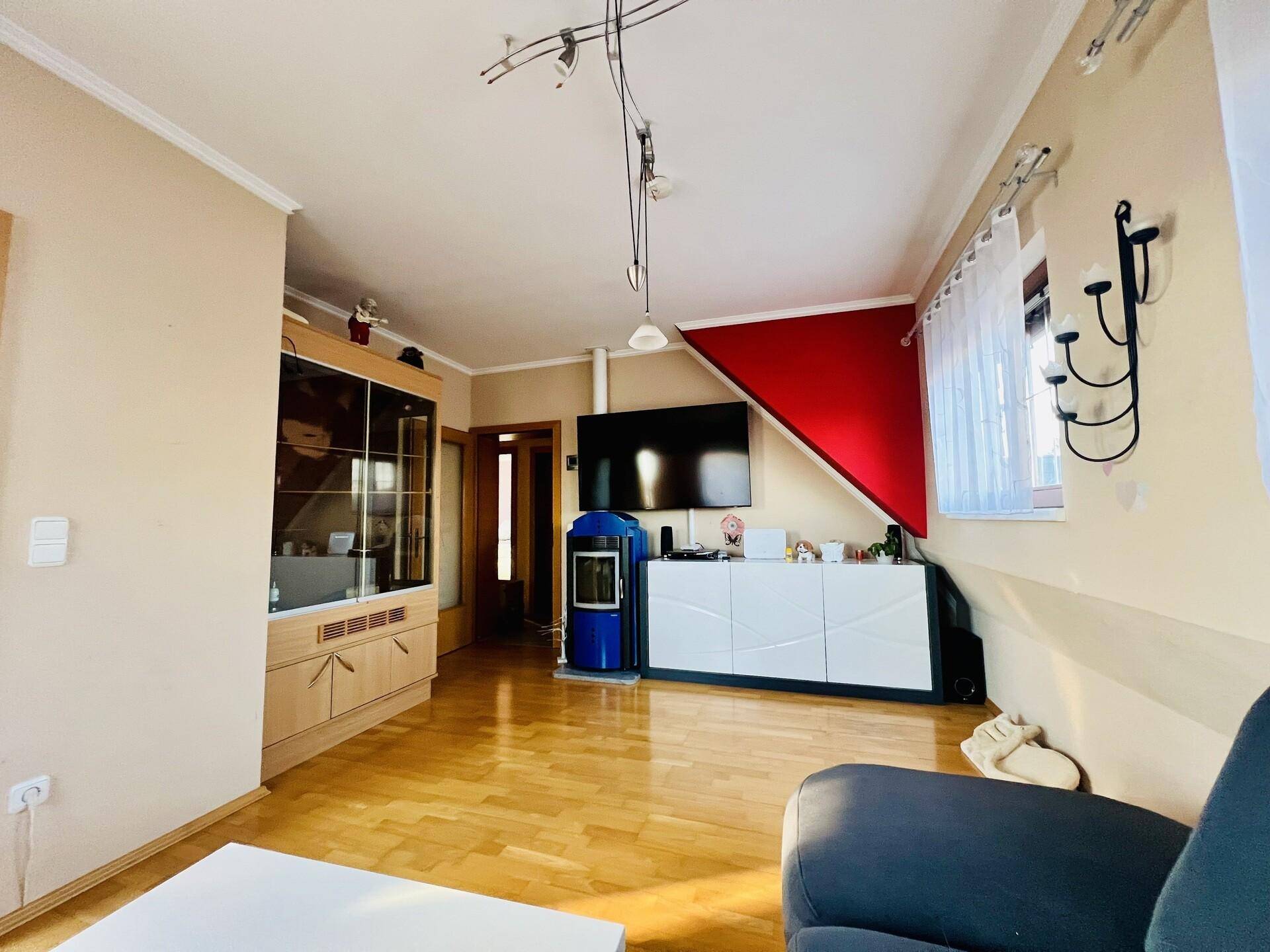 Gemütliches Wohnzimmer im Dachgeschoss mit Holzboden, Kaminofen und farbiger Akzentwand.