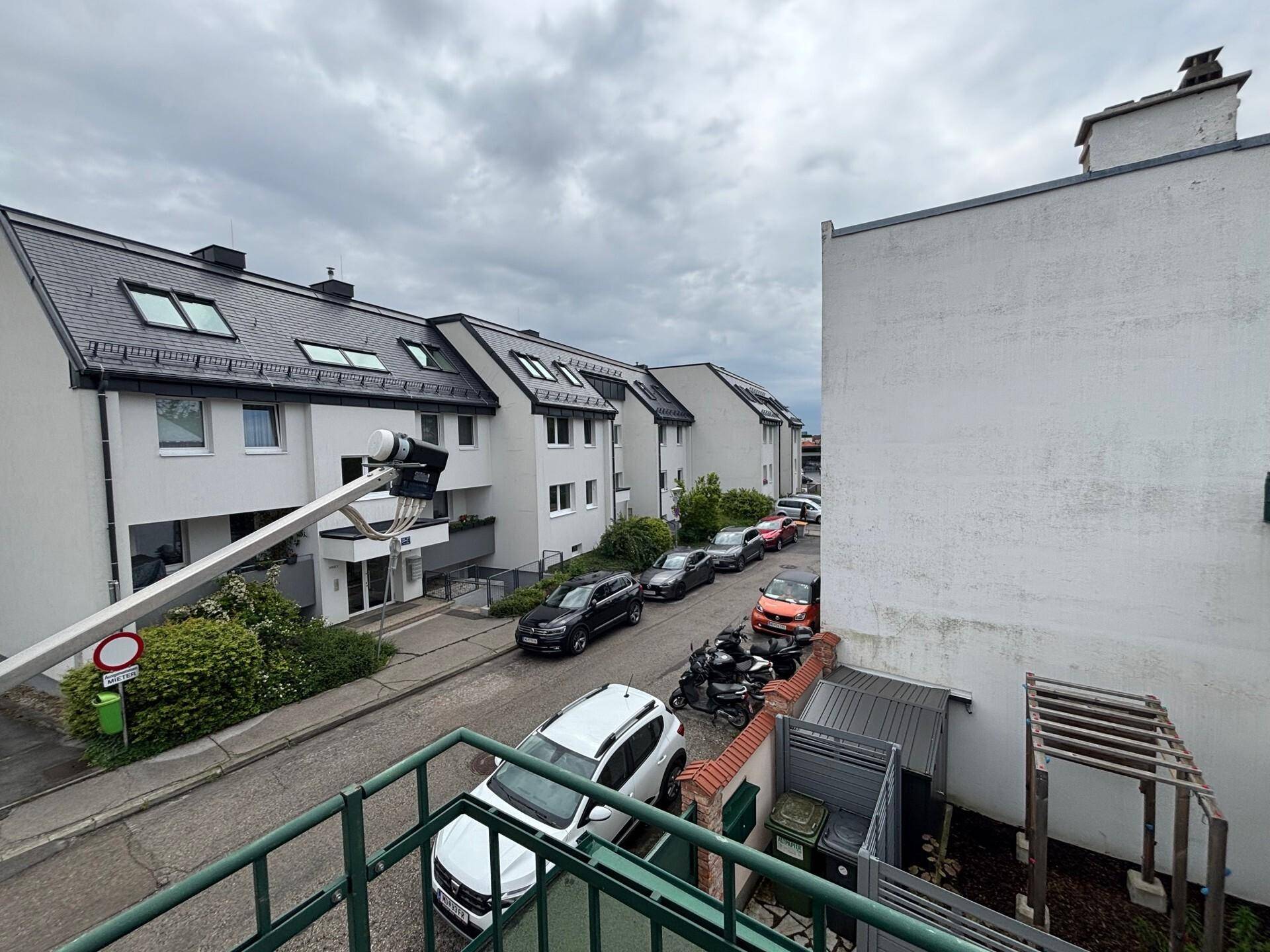 Blick vom Balkon auf eine Wohnstraße mit geparkten Autos und modernen Gebäuden.