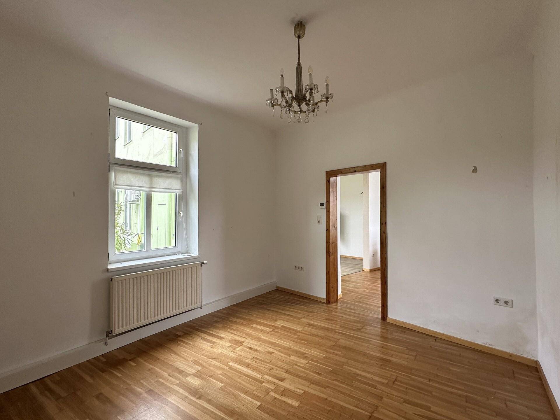 Helles Zimmer mit Parkettboden und Kronleuchter, ideal als Wohn- oder Schlafzimmer nutzbar.