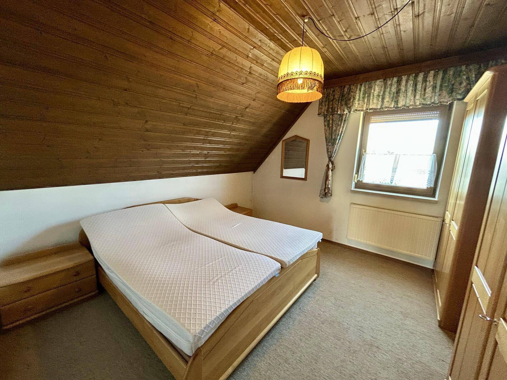 Schlafzimmer im Dachgeschoss mit Holzdecke, Teppichboden und Doppelbett.