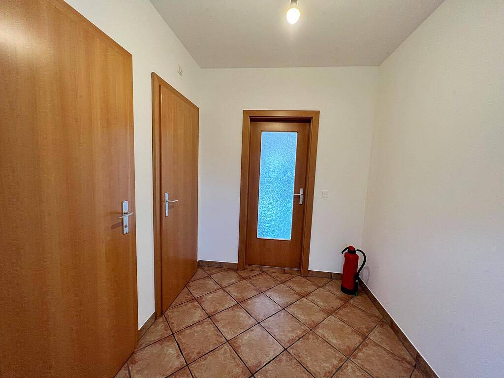 Heller Flur mit braunen Fliesen, zwei Holztüren und einem Feuerlöscher.