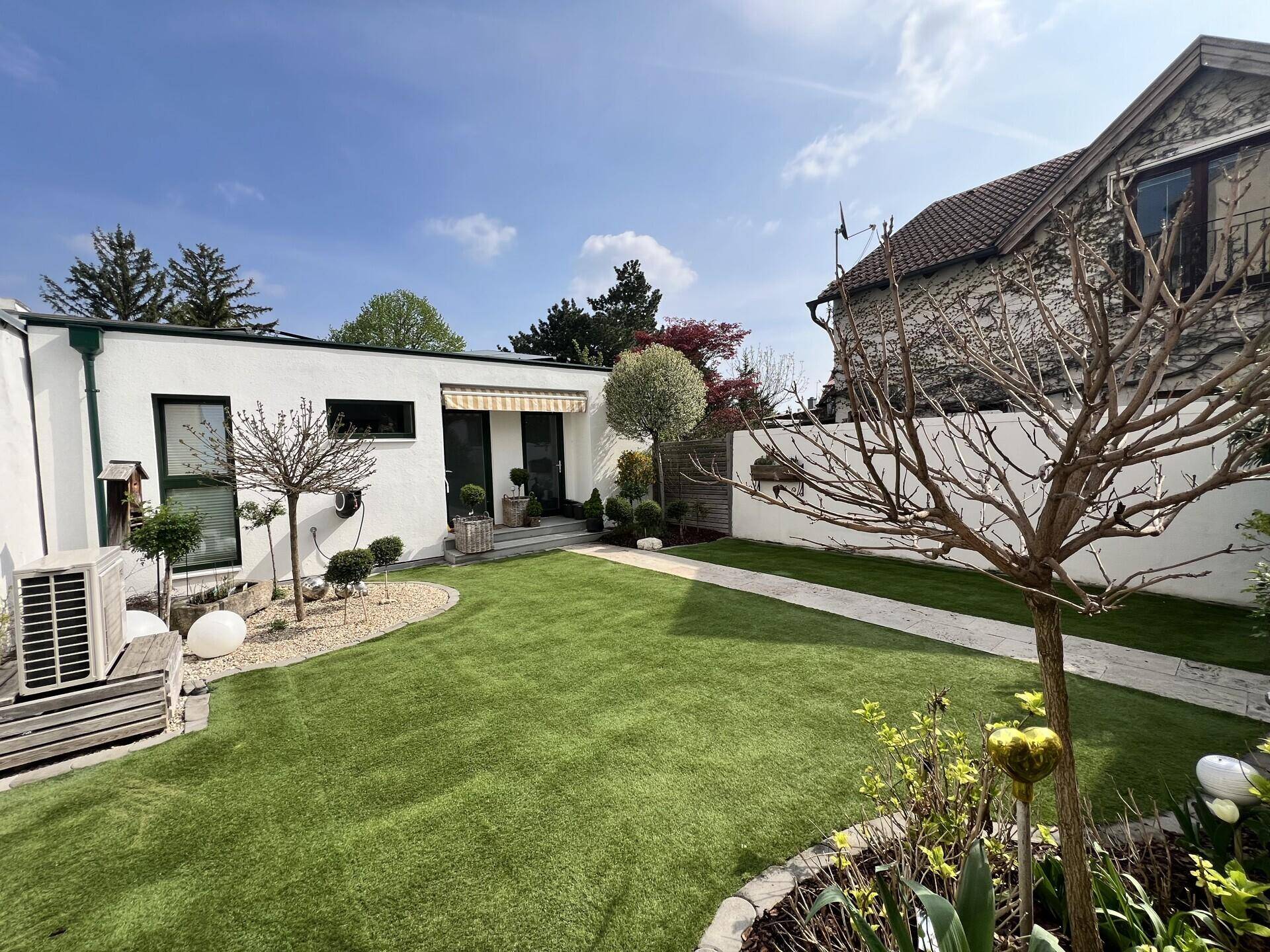 Weitläufiger Garten mit gepflegtem Rasen, Steinweg und verschiedenen Zierbäumen.