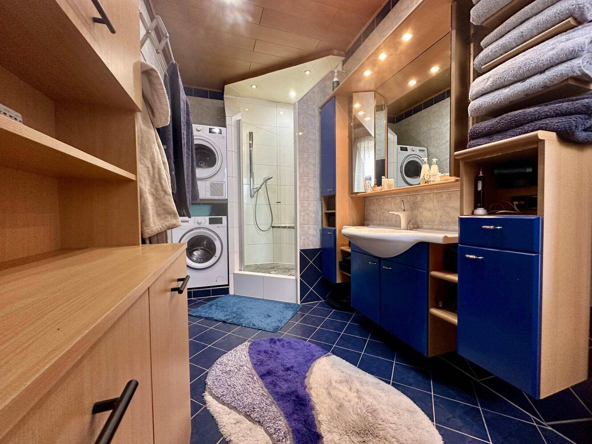 Badezimmer mit blauen Fliesen, Waschbecken, Spiegel und Holzschränken für Handtücher.