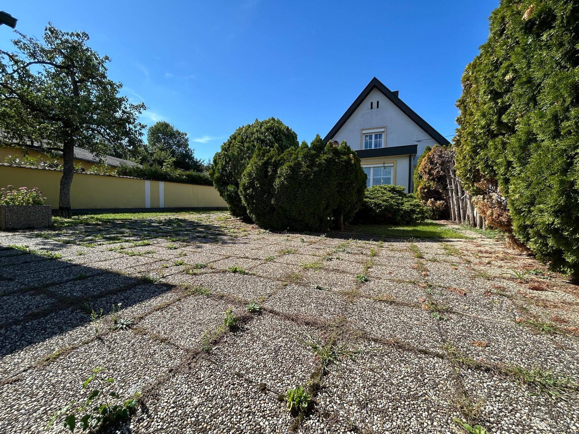 Rückansicht des Hauses mit großem gepflasterten Bereich und grüner Bepflanzung.