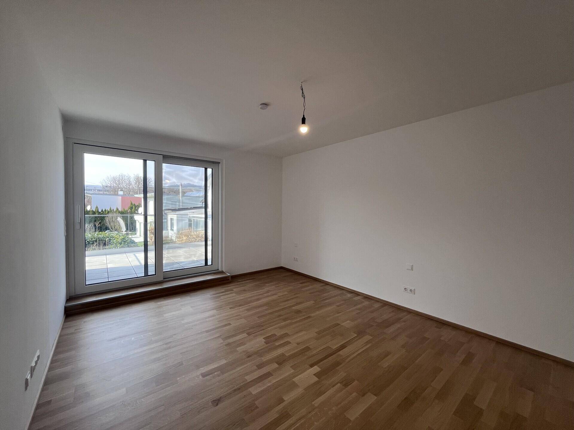 Helles Schlafzimmer mit Parkettboden und Schiebetür zum Außenbereich.