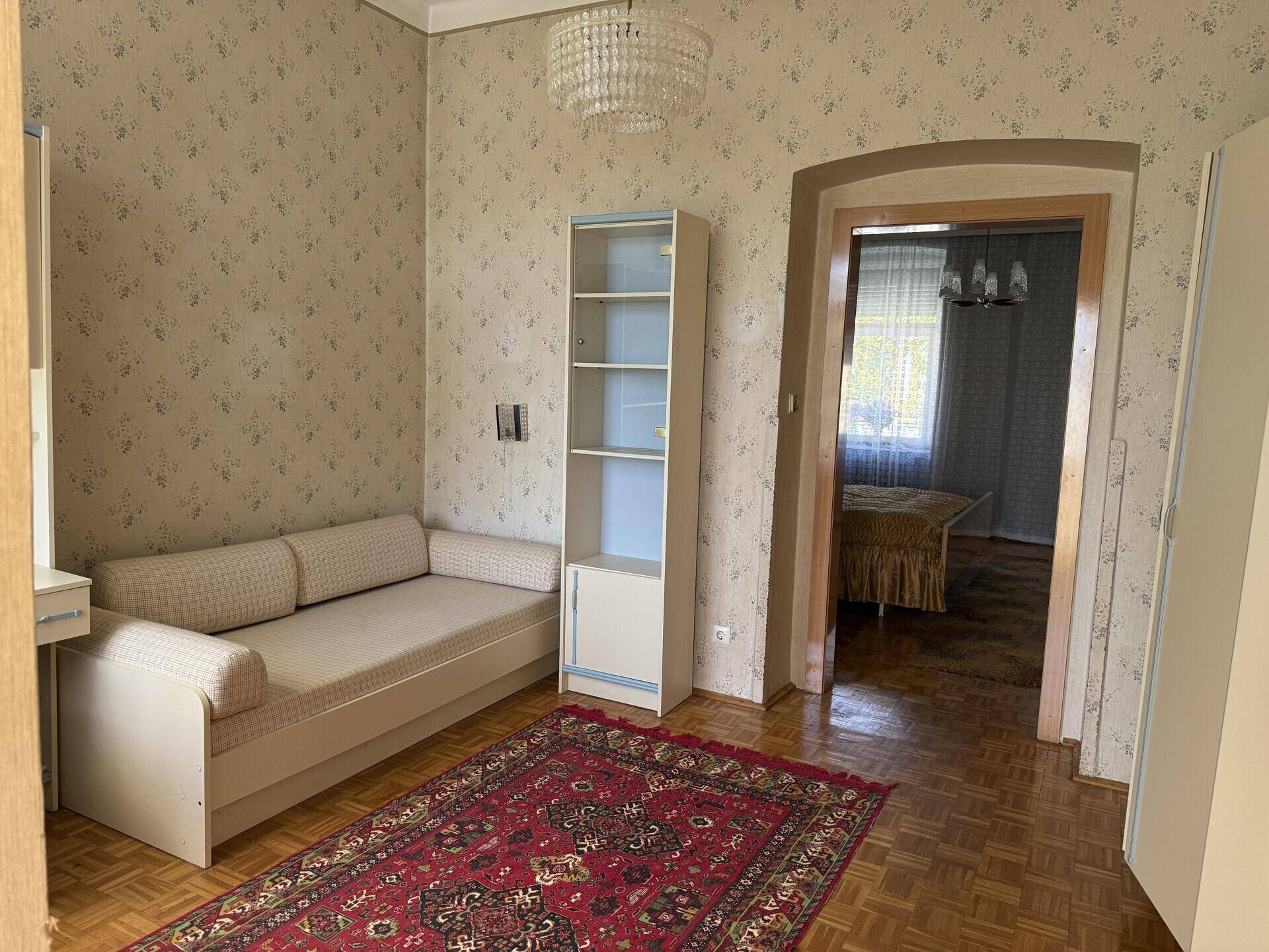 Schlafzimmer mit Parkettboden, Tagesbett und einem Bücherregal, das Stauraum bietet.